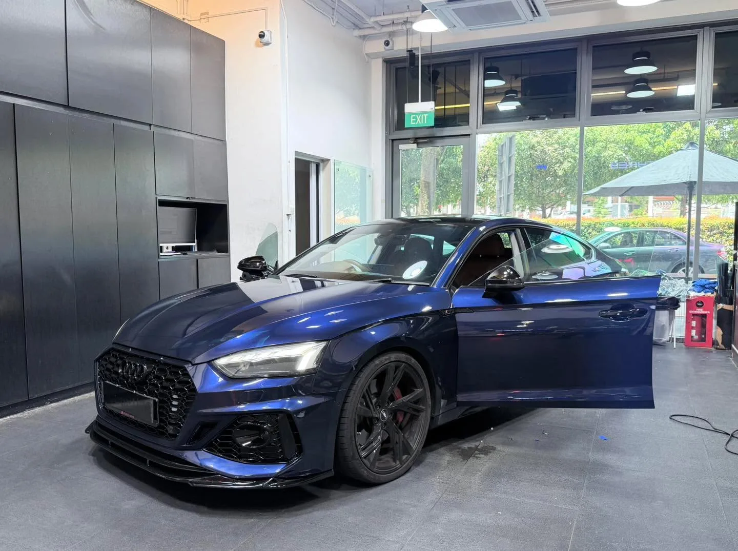 A blue sedan with doors open, positioned indoors at the workshop with tools and equipment visible.
