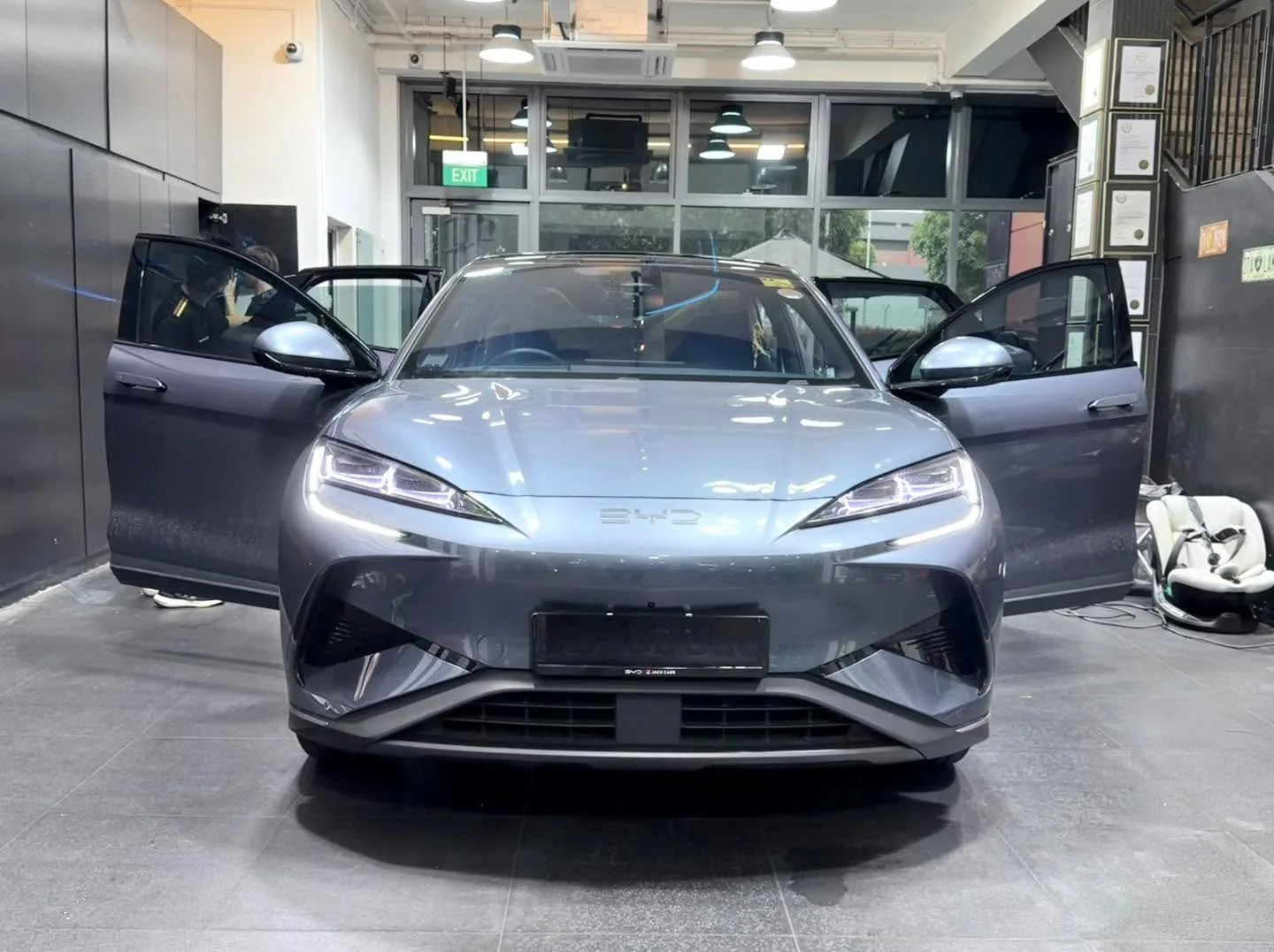 A silver electric sedan with distinctive split headlights, viewed from the front with both doors open.