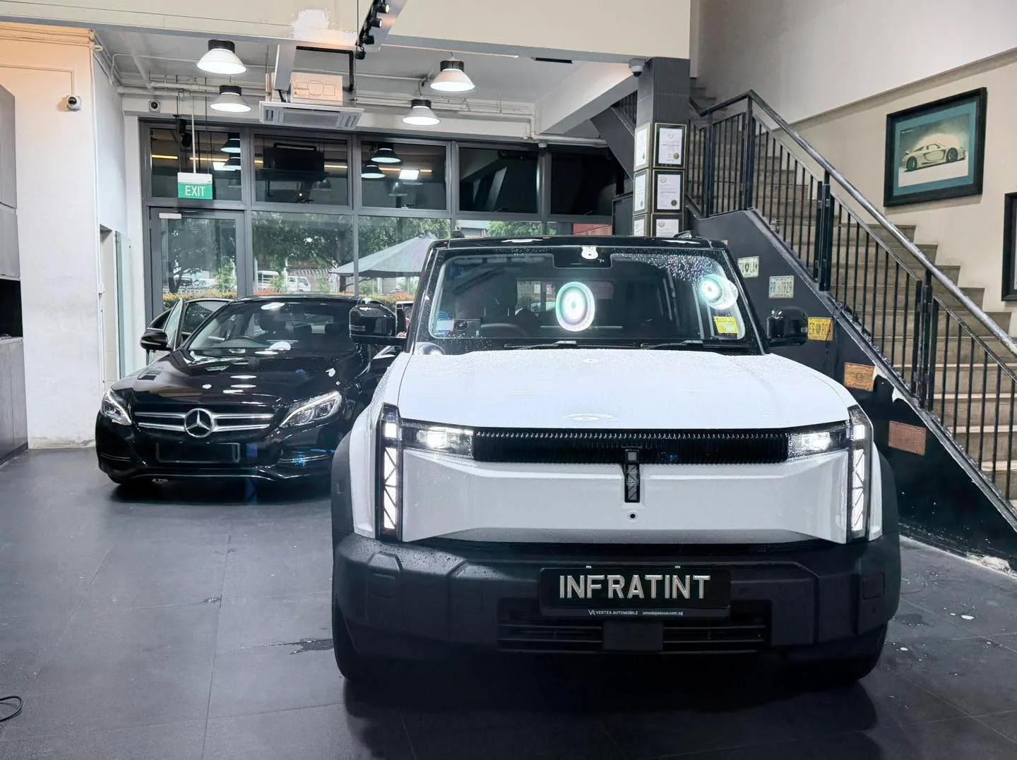 A white electric SUV with Infratint branding and a black Mercedes-Benz sedan inside the workshop.