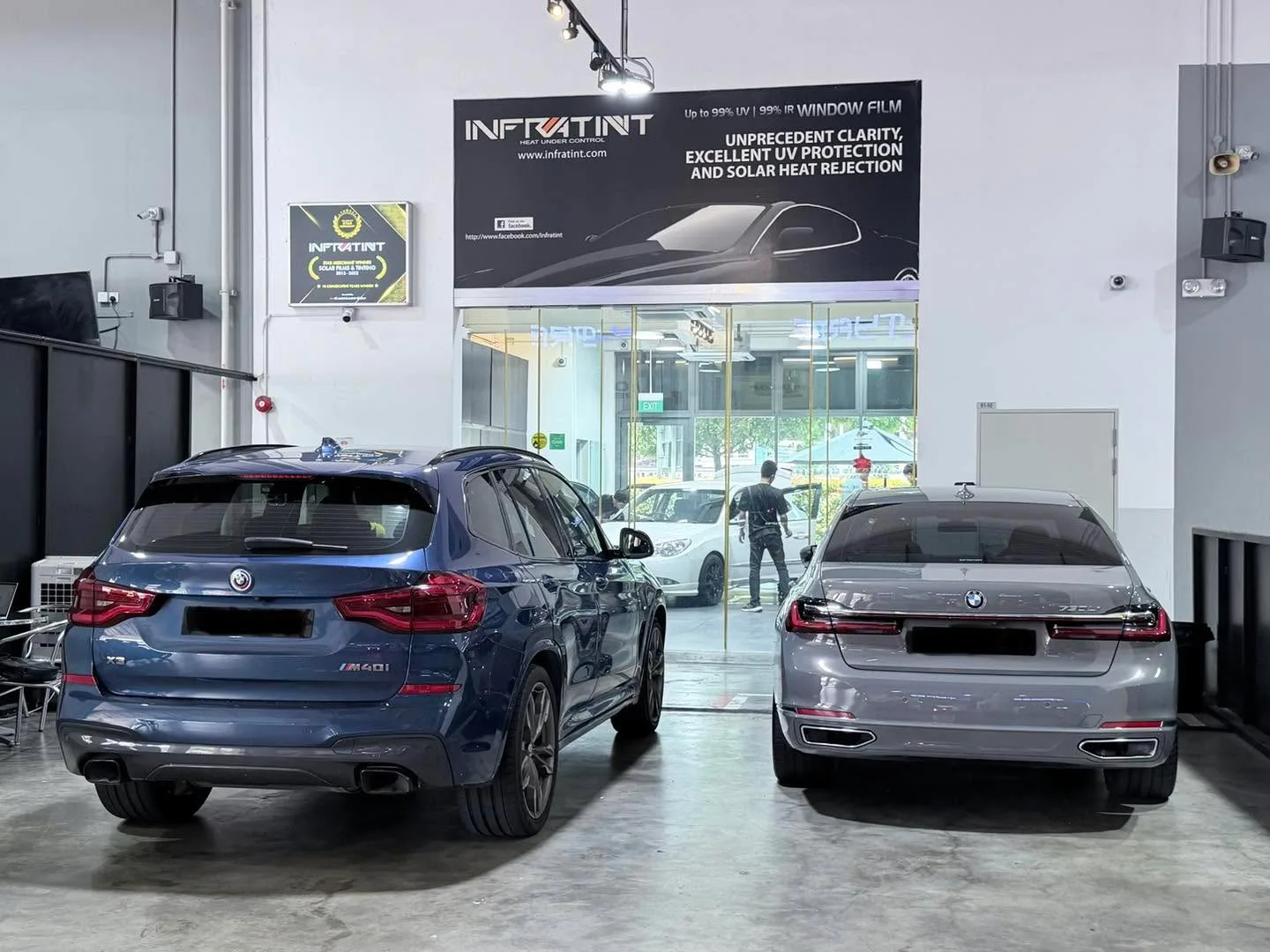 A blue BMW X3 SUV and a grey BMW sedan parked in the Infratint workshop.