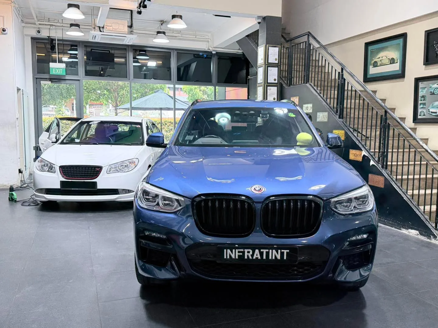A blue BMW X3 SUV parked in the workshop interior near white walls.