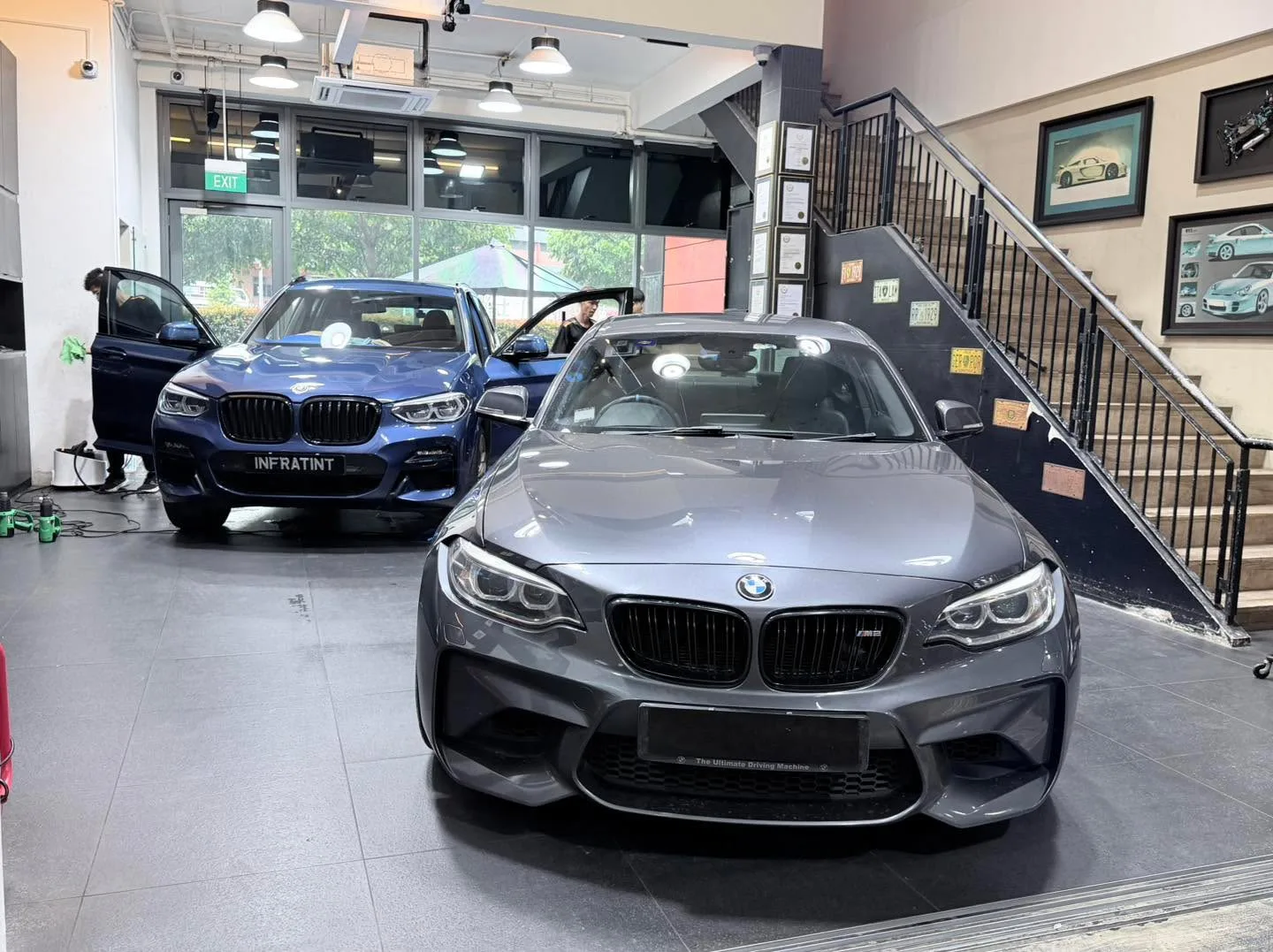 A grey BMW sedan and a blue BMW X3 in the workshop during tinting.
