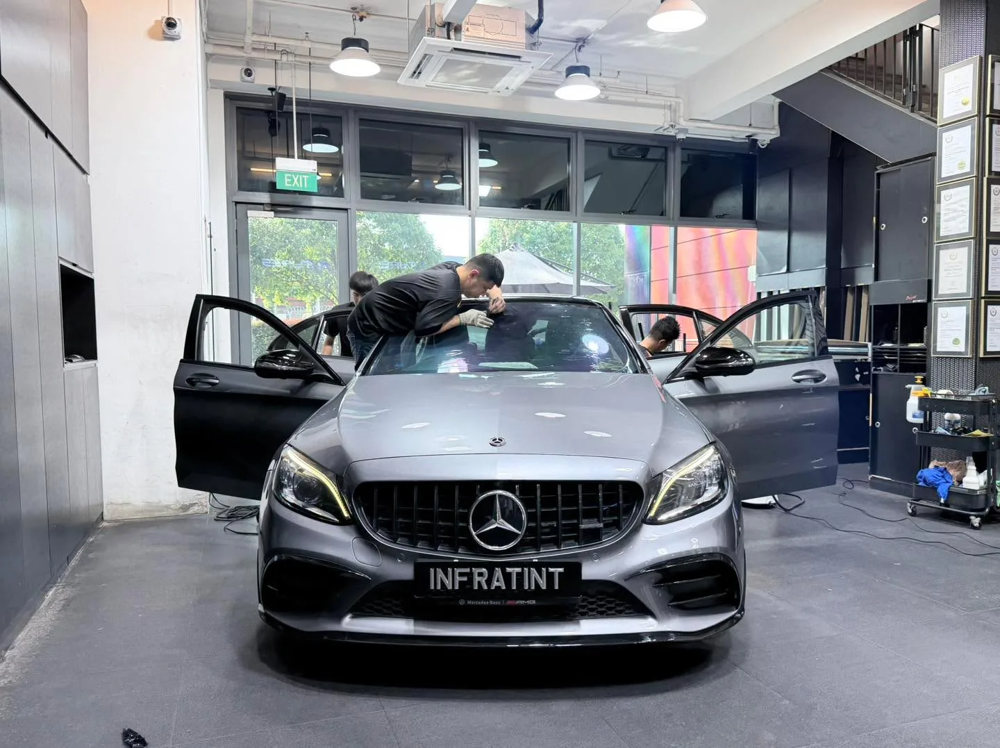 A silver Mercedes-Benz sedan with an open door and technician inspecting the windscreen.