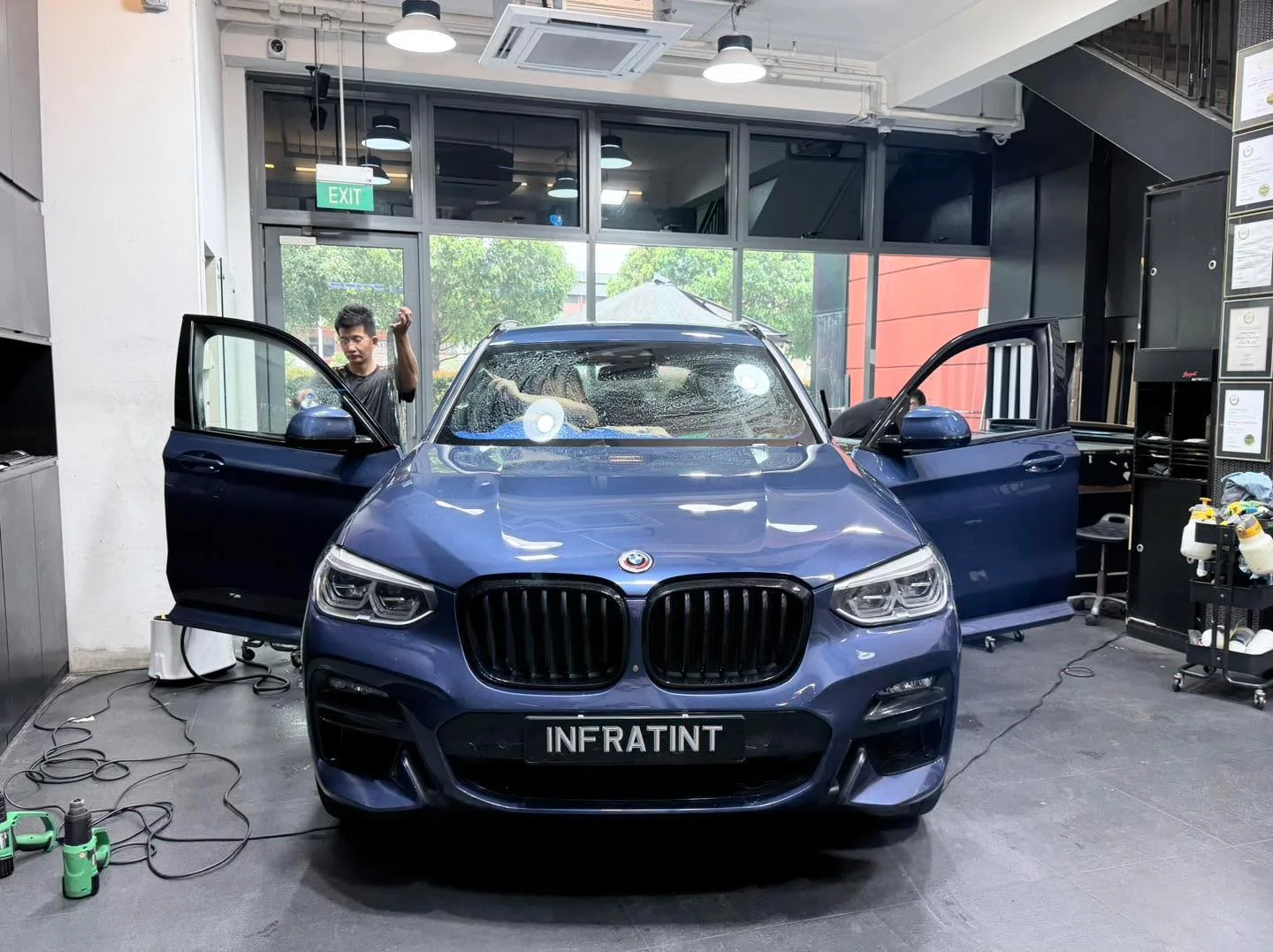 A white sedan with open doors being tinted in the workshop.