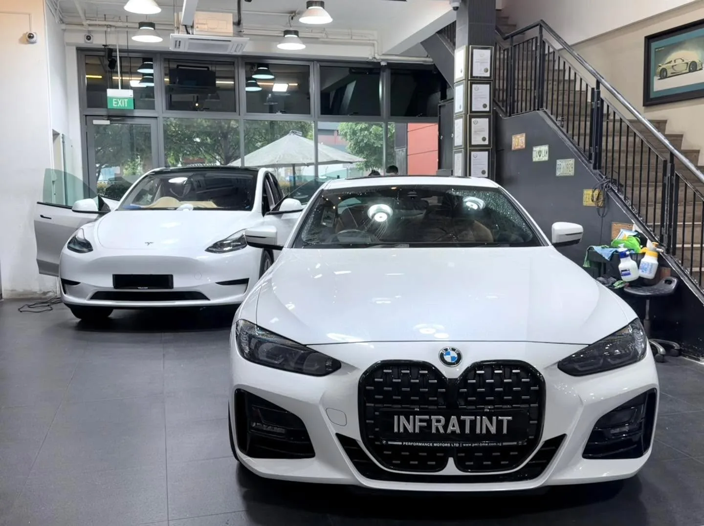 A white BMW M4 coupe and a white Tesla sedan inside the workshop, with staff present.