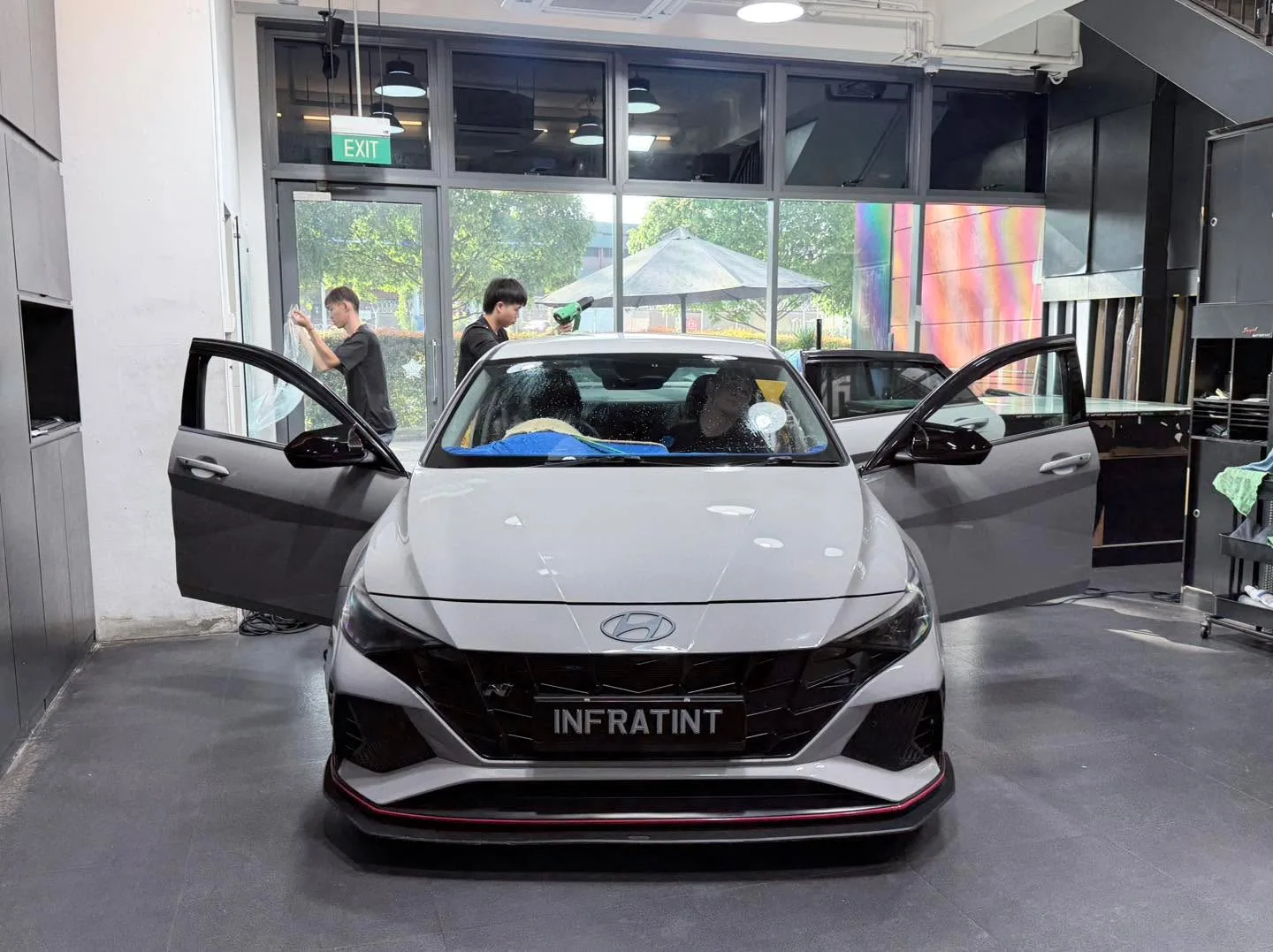 A white Hyundai Avante sedan with both rear doors open, showing technicians applying tint film.