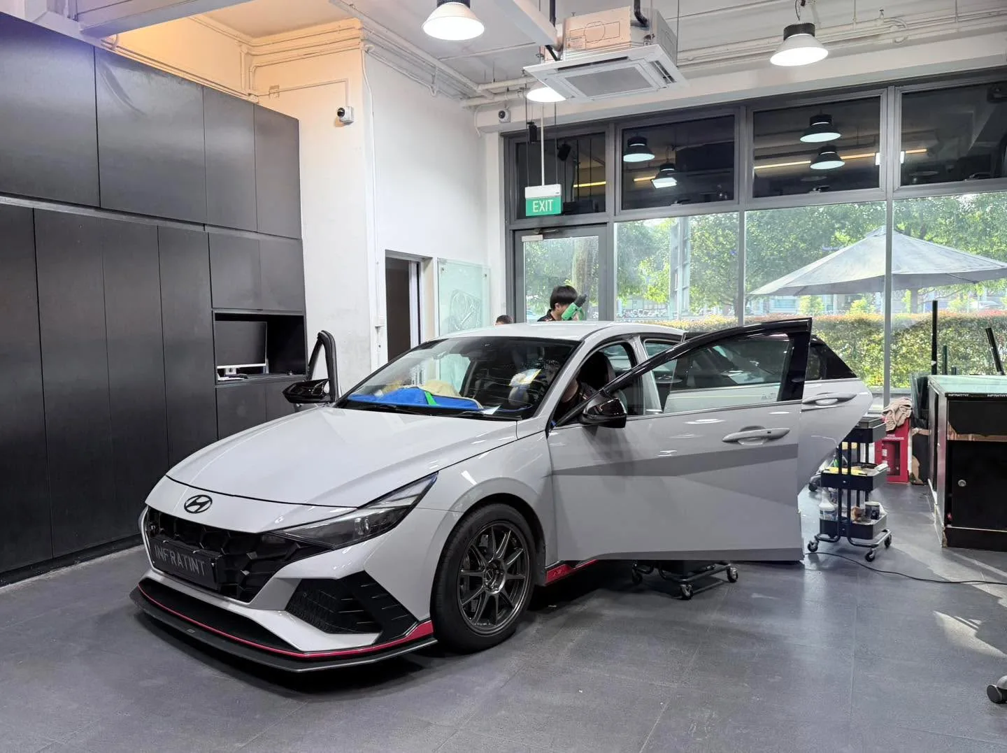 A white Hyundai Avante sedan with doors open, workstation visible with tools and equipment nearby.