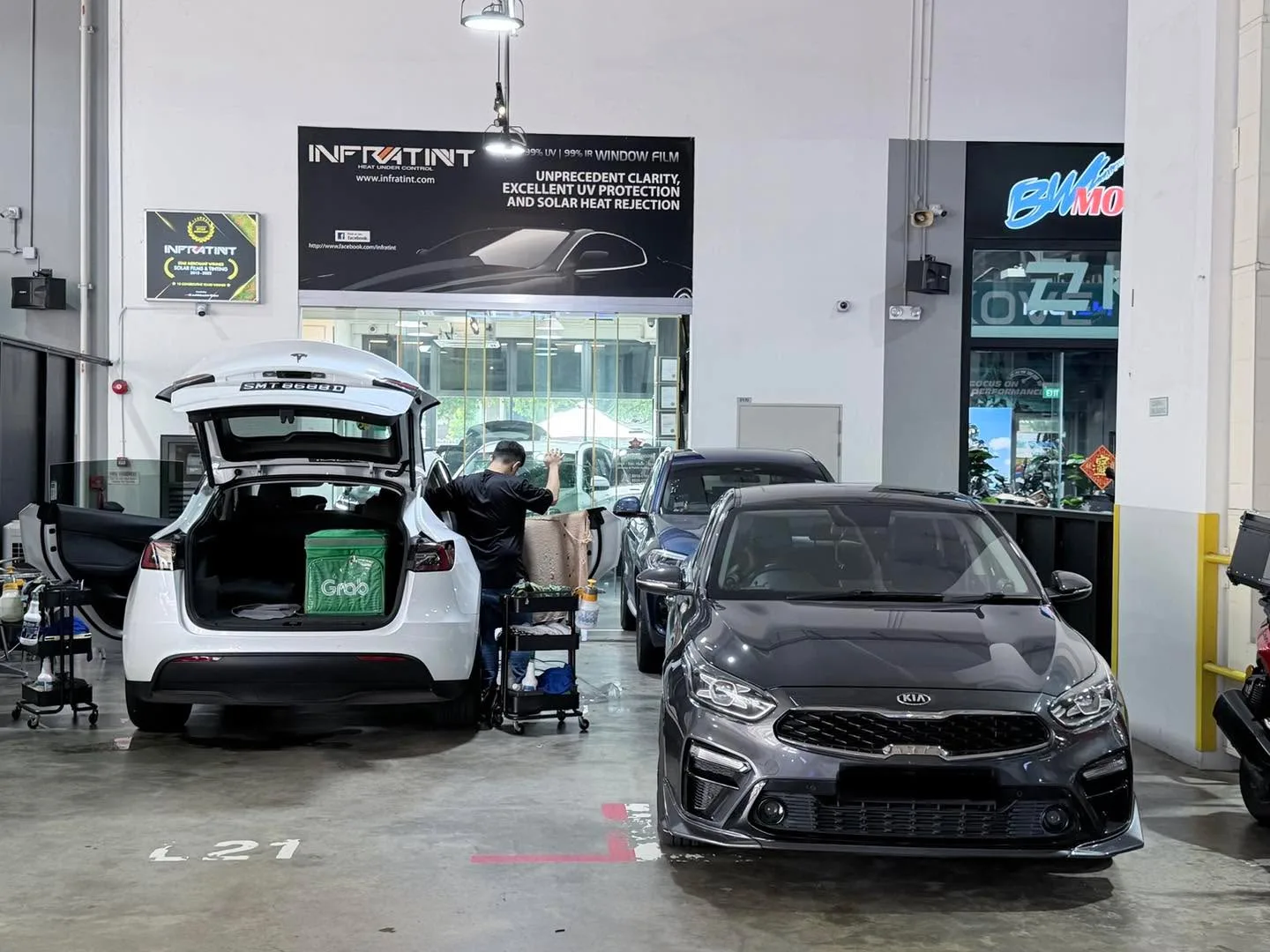 A white Tesla Model Y and a black Kia Cerato inside the workshop.