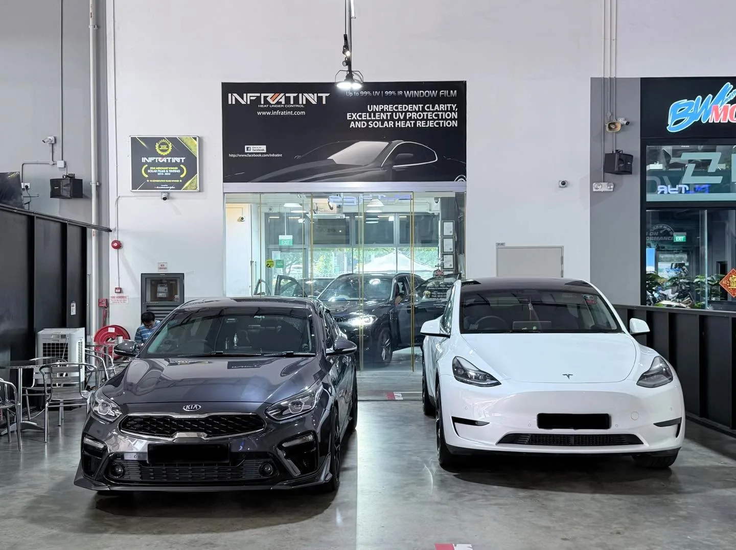 A white Tesla Model Y and a dark Kia Cerato parked in the workshop.