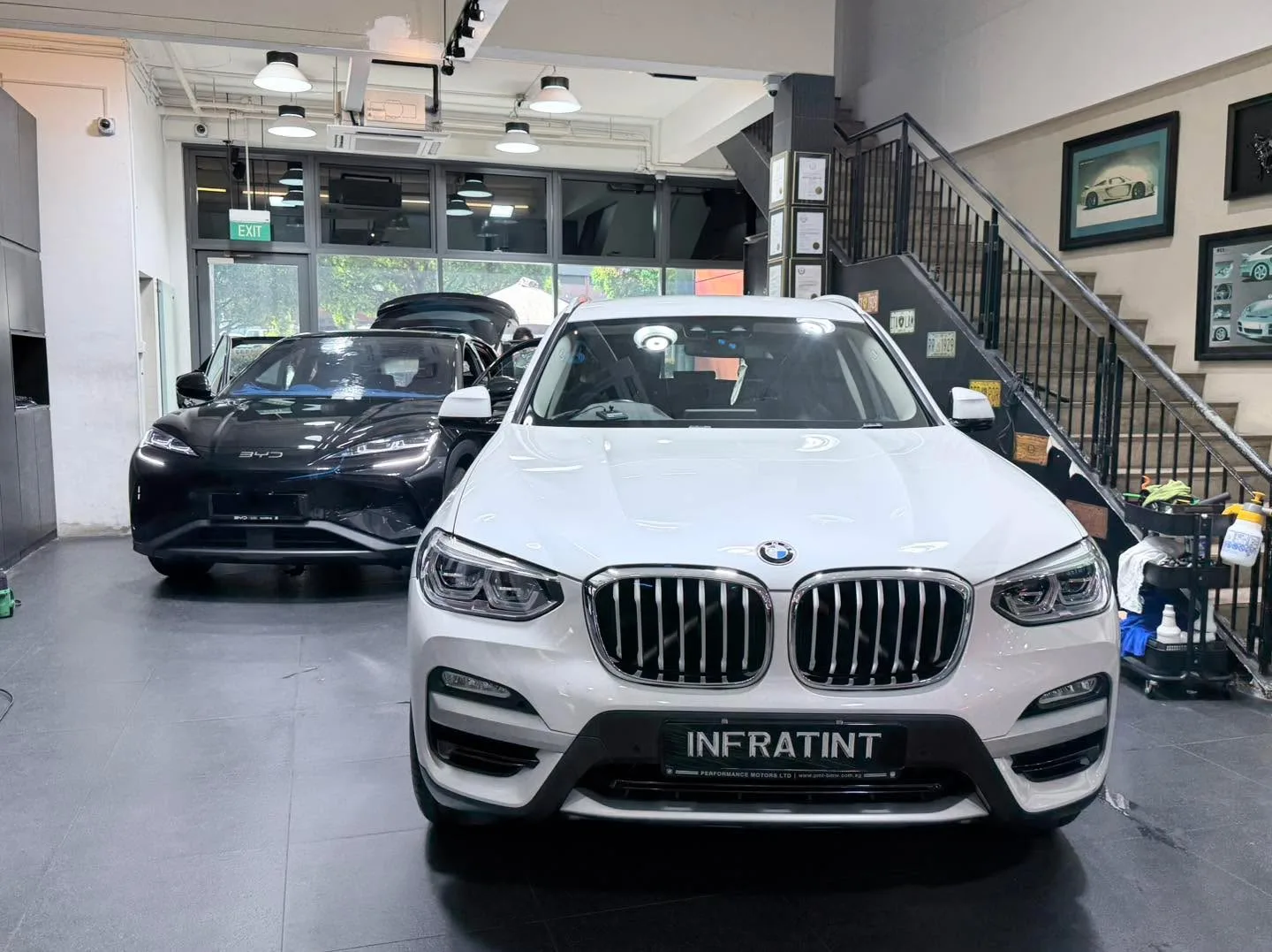 A white BMW X3 and a black Tesla Model Y at the workshop entrance.