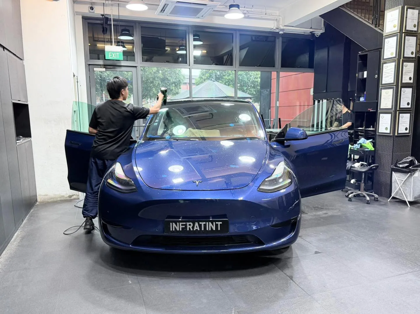 A dark Tesla Model Y with doors open during tinting service.