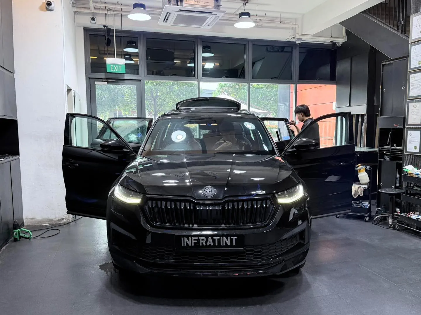 A black Škoda Kodiaq with both front doors open, viewed head-on in the workshop.