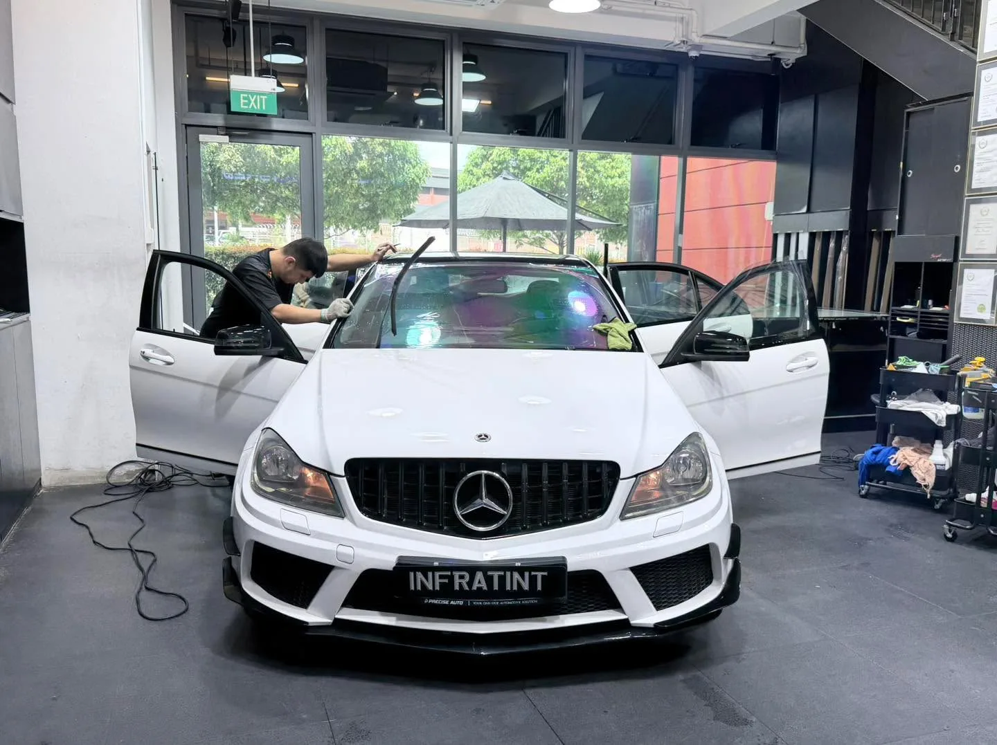 A white Mercedes-Benz C-Class with both front doors open as technician applies window film.