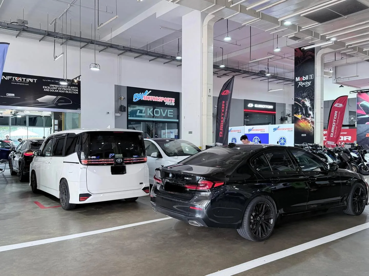 A white BYD Sealion 7 and a black BMW parked indoors at a workshop.