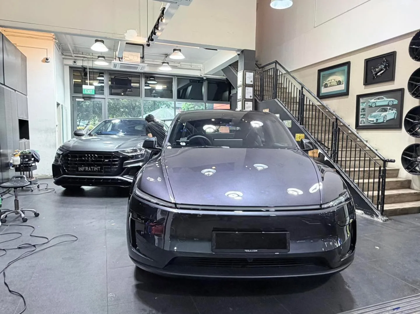 A dark grey Tesla Model Y parked indoors at a workshop.
