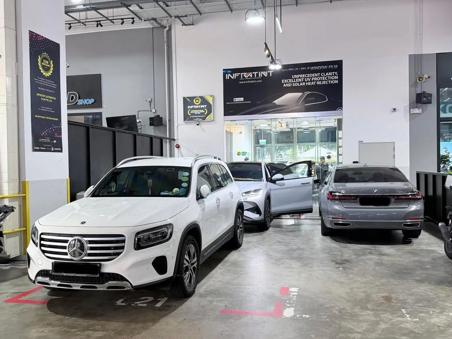 A white Mercedes-Benz GLB, a white Tesla Model Y sedan, and a silver BMW saloon parked in the workshop.