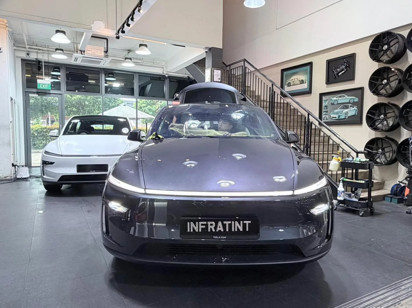 A black Maserati GranTurismo sports car parked in the workshop with a white vehicle behind it.