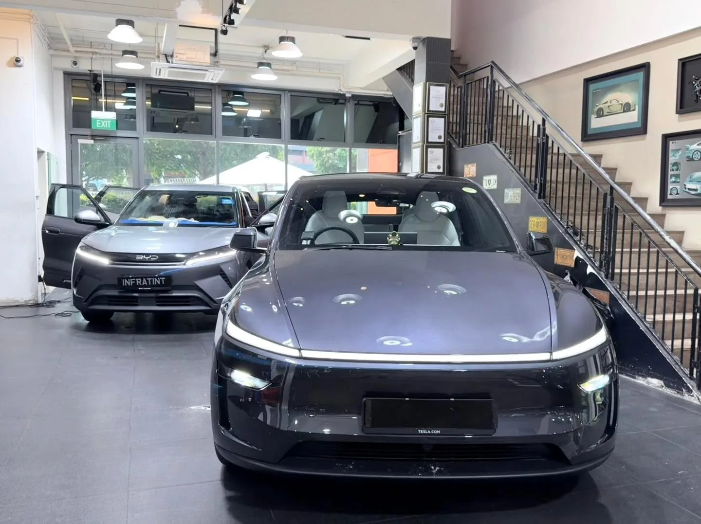 A black Tesla Model Y and a black Maserati GranTurismo parked in the workshop.