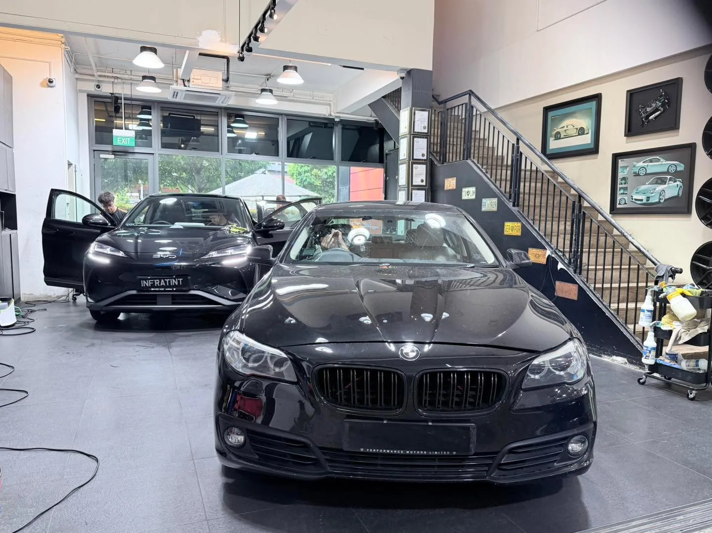A black BMW saloon and a black Maserati GranTurismo parked in the workshop.