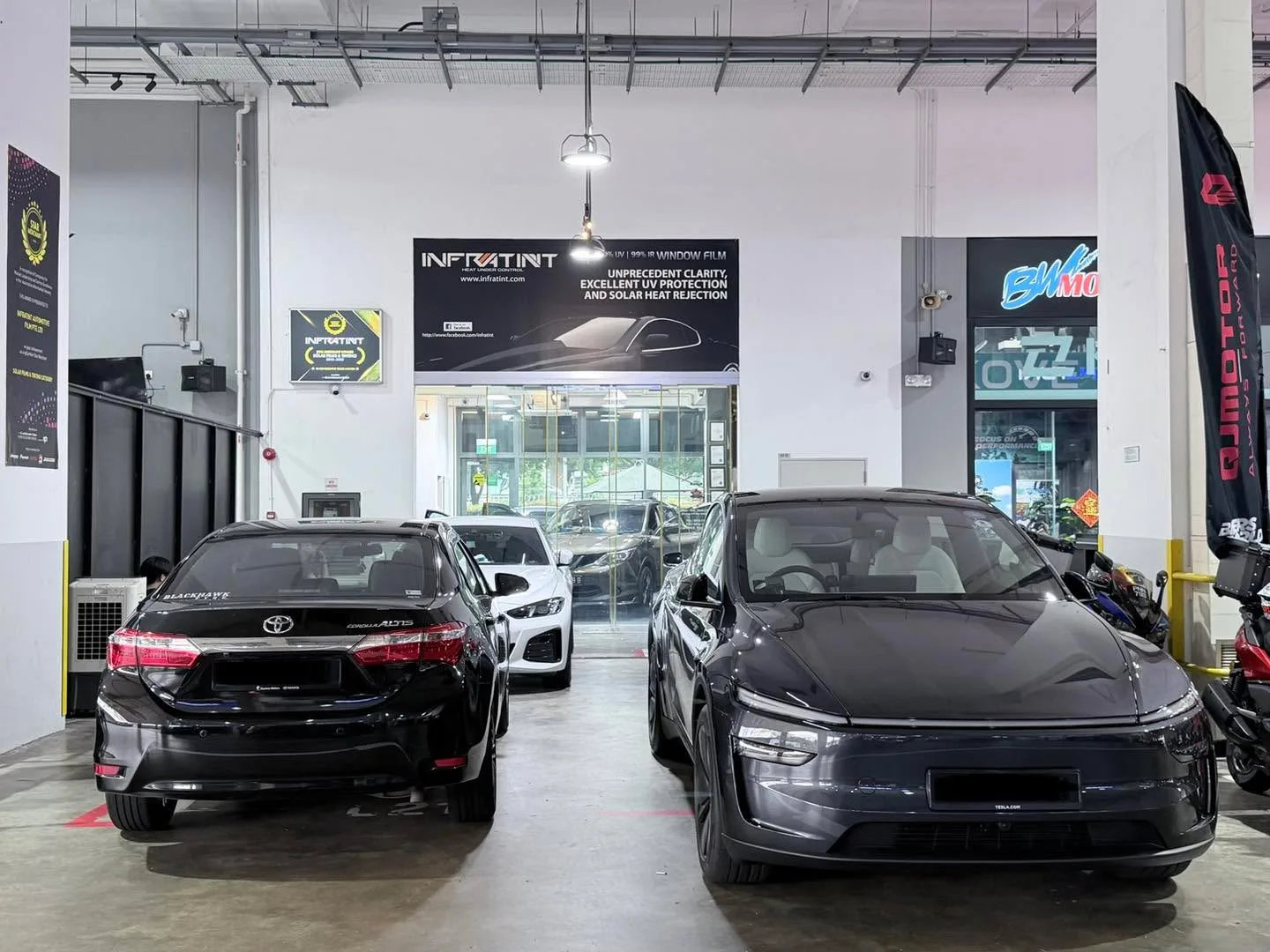 A black Toyota Corolla sedan and dark grey electric sedan inside the workshop.