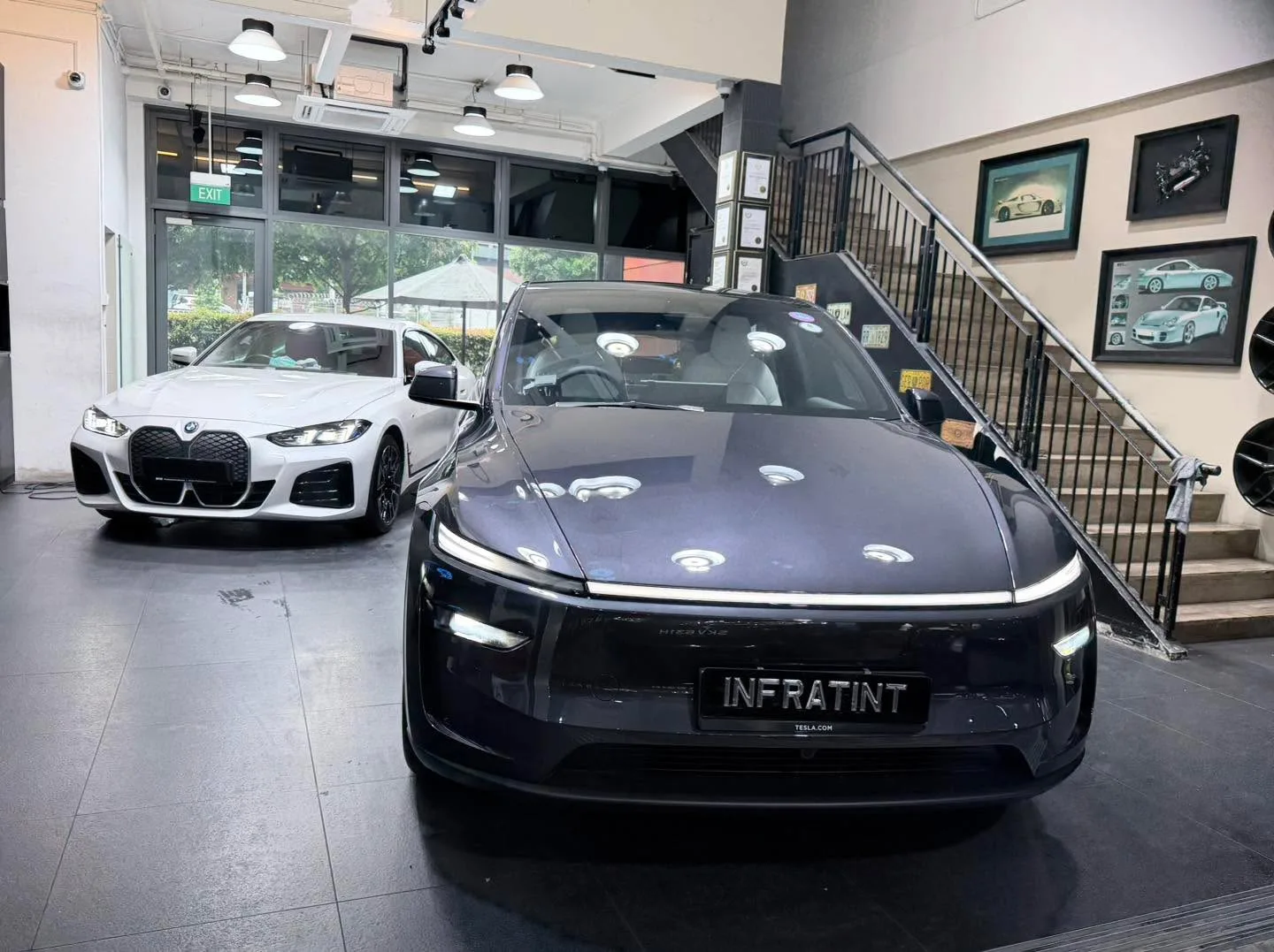 A dark grey electric sedan with Infratint branding and a white BMW coupe.