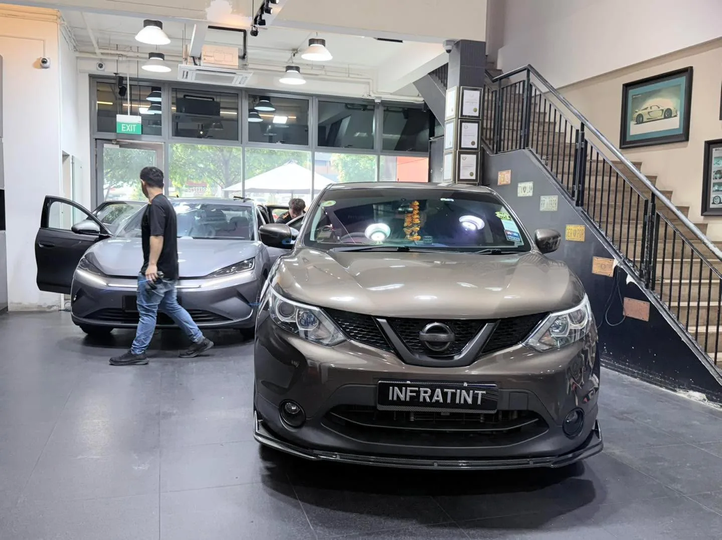 A grey sedan with workers beside it inside the workshop.