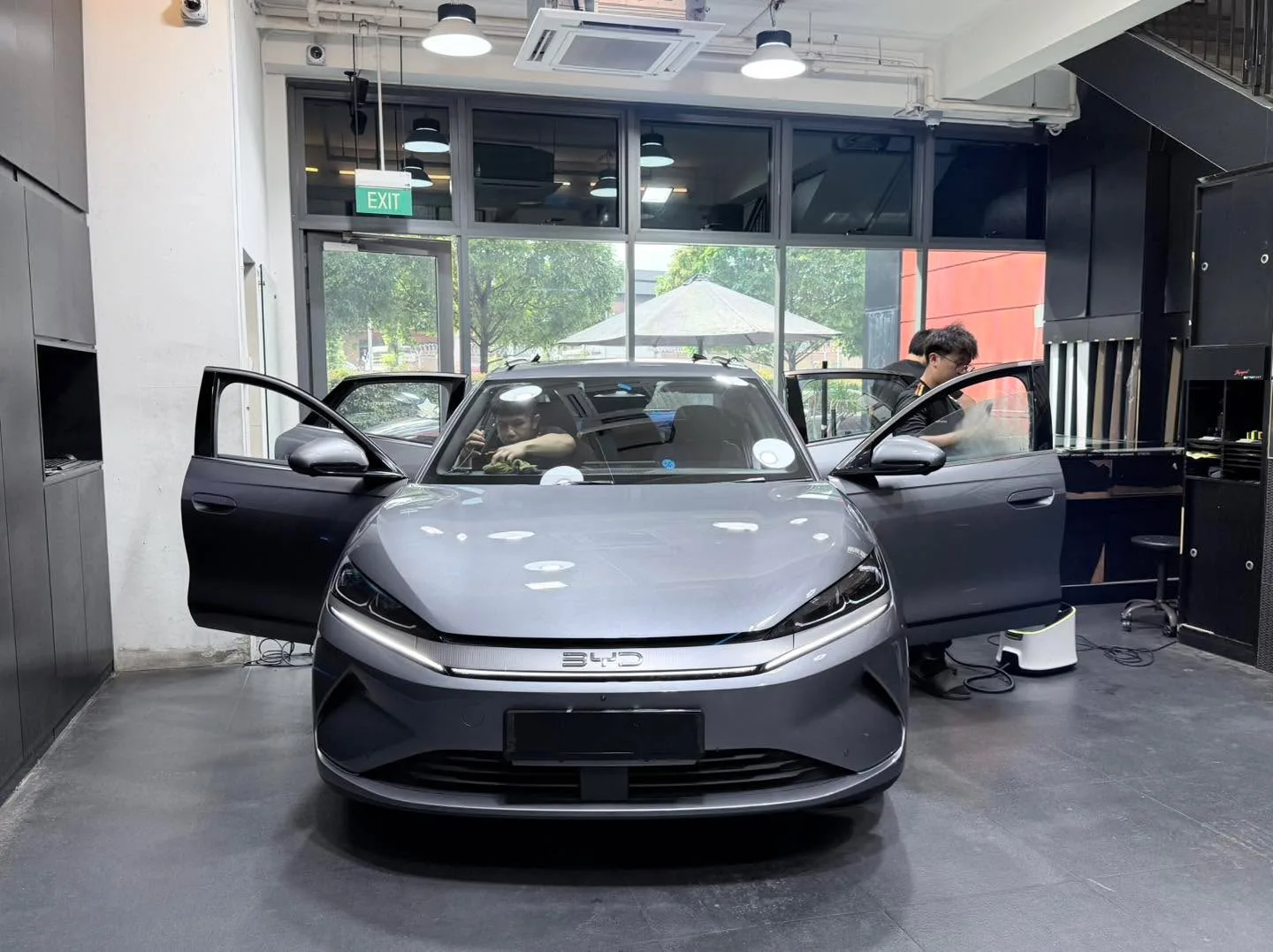 A grey BYD sedan with both doors open inside the workshop.