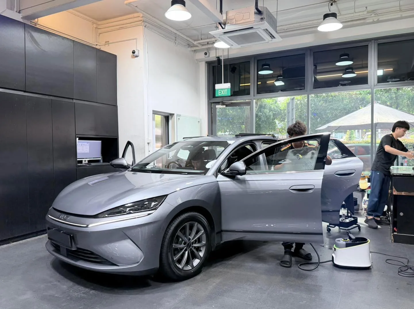A silver BYD sedan with doors open during window tinting work.