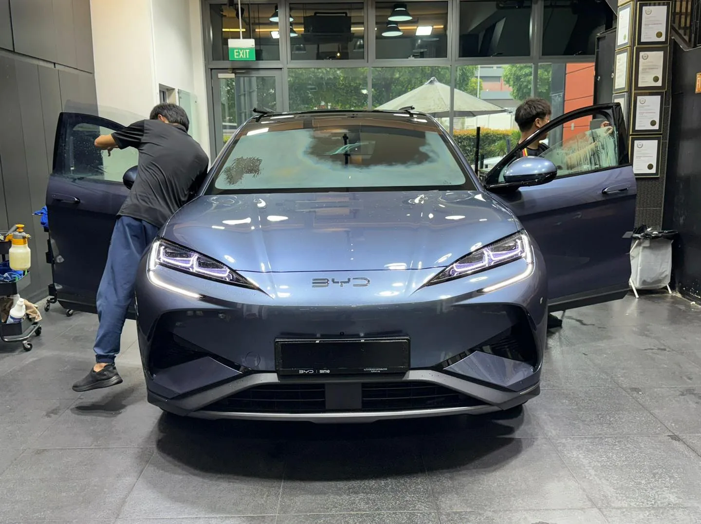 A grey BYD sedan with workers applying window film.