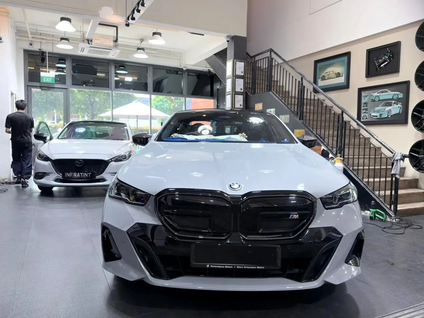 A white BMW with a distinctive large grille and a white Mazda 3 hatchback parked indoors at Infratint.