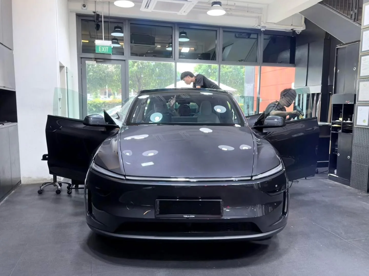 A dark grey Tesla sedan with doors open, staff applying window film at the workshop.