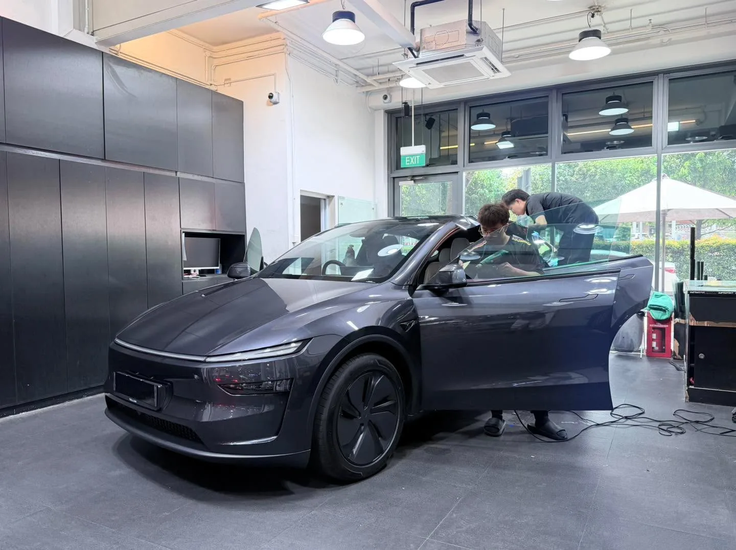 A dark grey Tesla sedan with open doors during window tinting, technicians working on the windows.