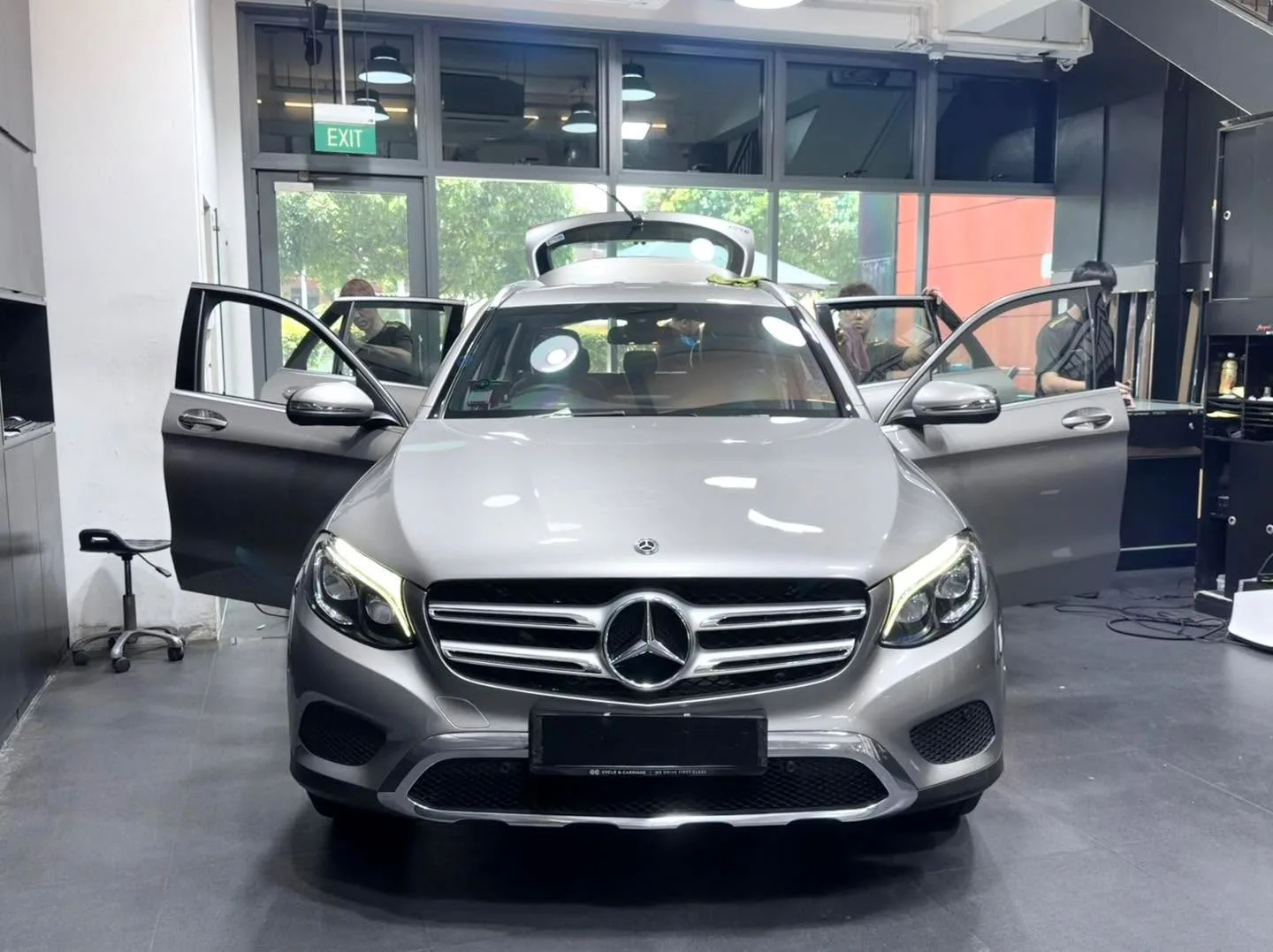 A silver Mercedes-Benz SUV with doors open at the workshop, staff tinting the windows.
