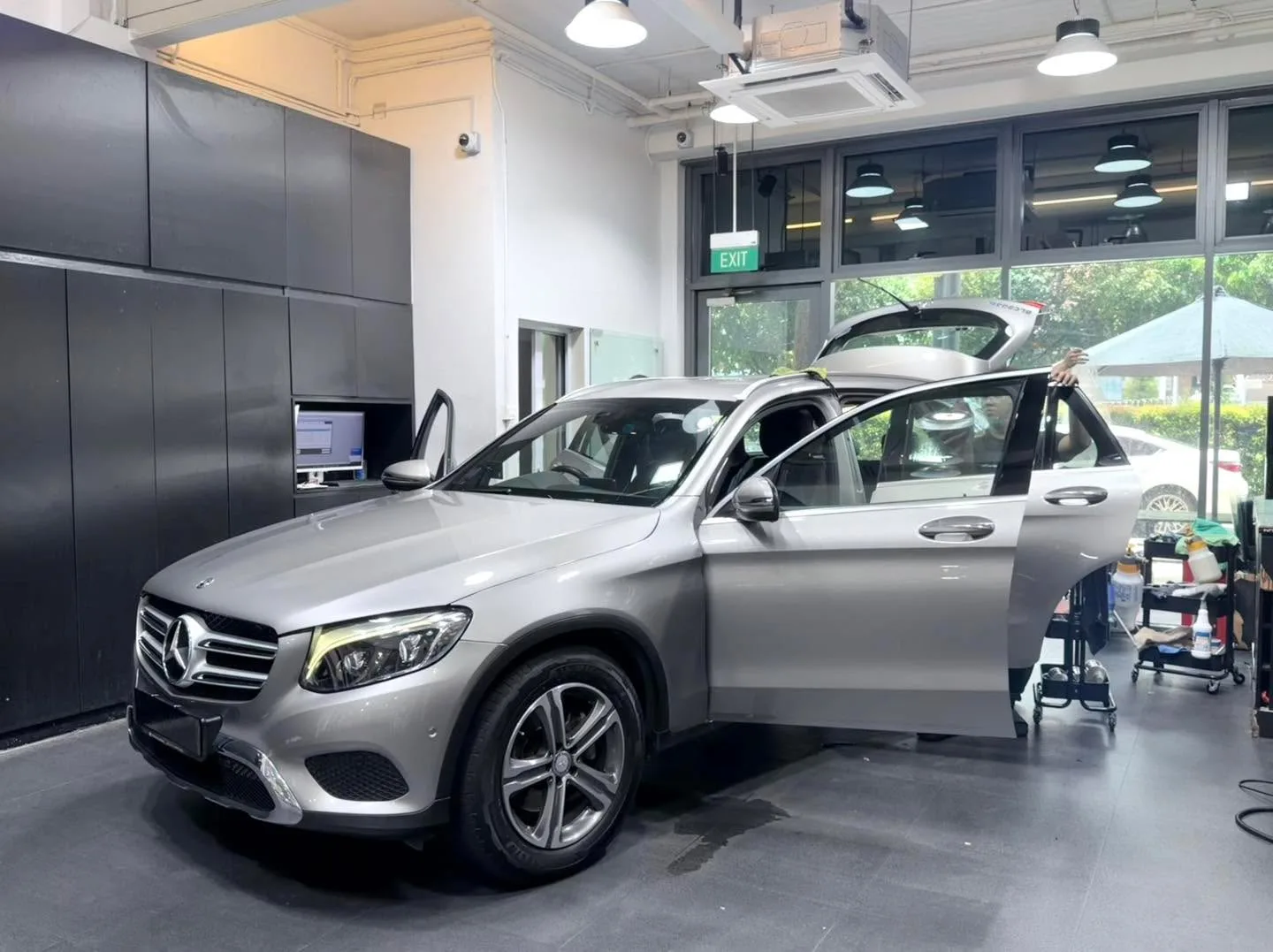 A silver Mercedes-Benz GLC SUV parked indoors with both doors open, window tinting in process.