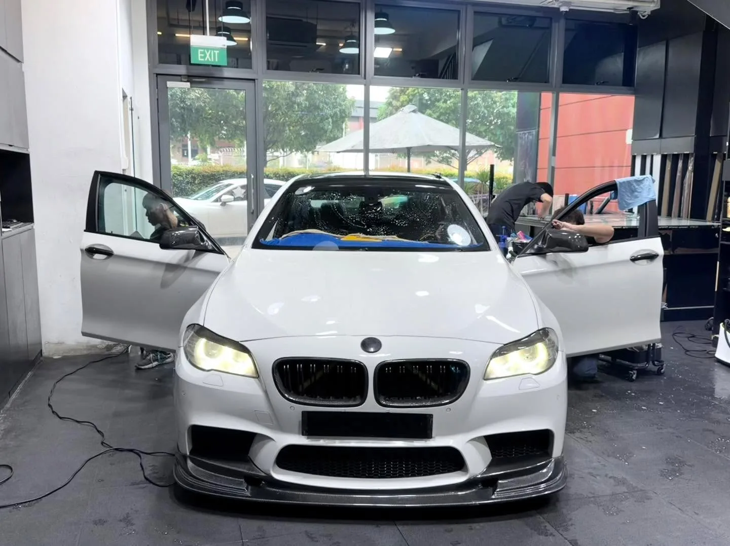 A white BMW saloon with doors fully open, technicians applying window film inside the workshop.
