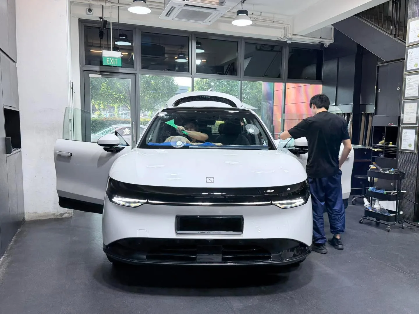 A white Zeekr electric SUV with doors open, staff applying window tint at the workshop.