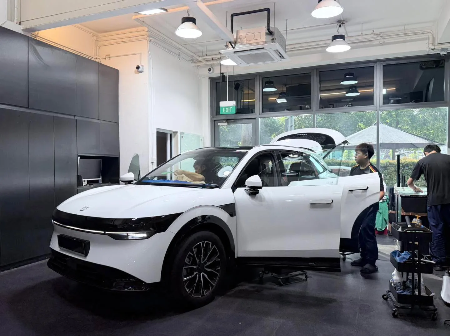 A white Skoda SUV with a door open, technicians working on the windows inside the workshop.