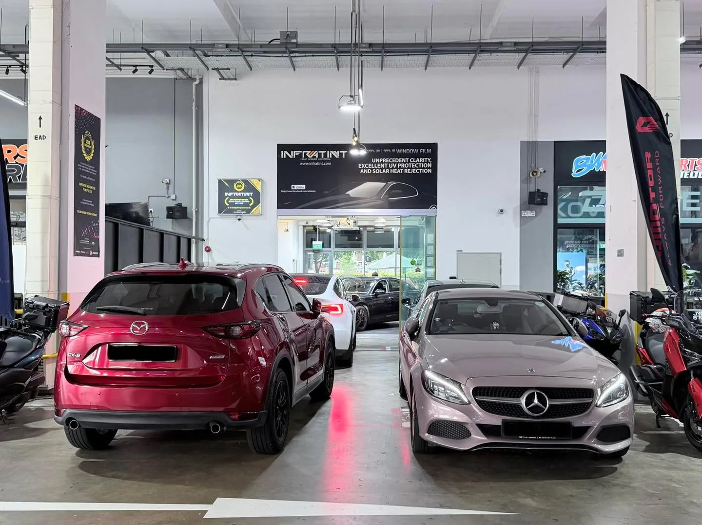 A red Mazda CX-5 SUV and a silver Mercedes-Benz saloon parked indoors at the workshop.
