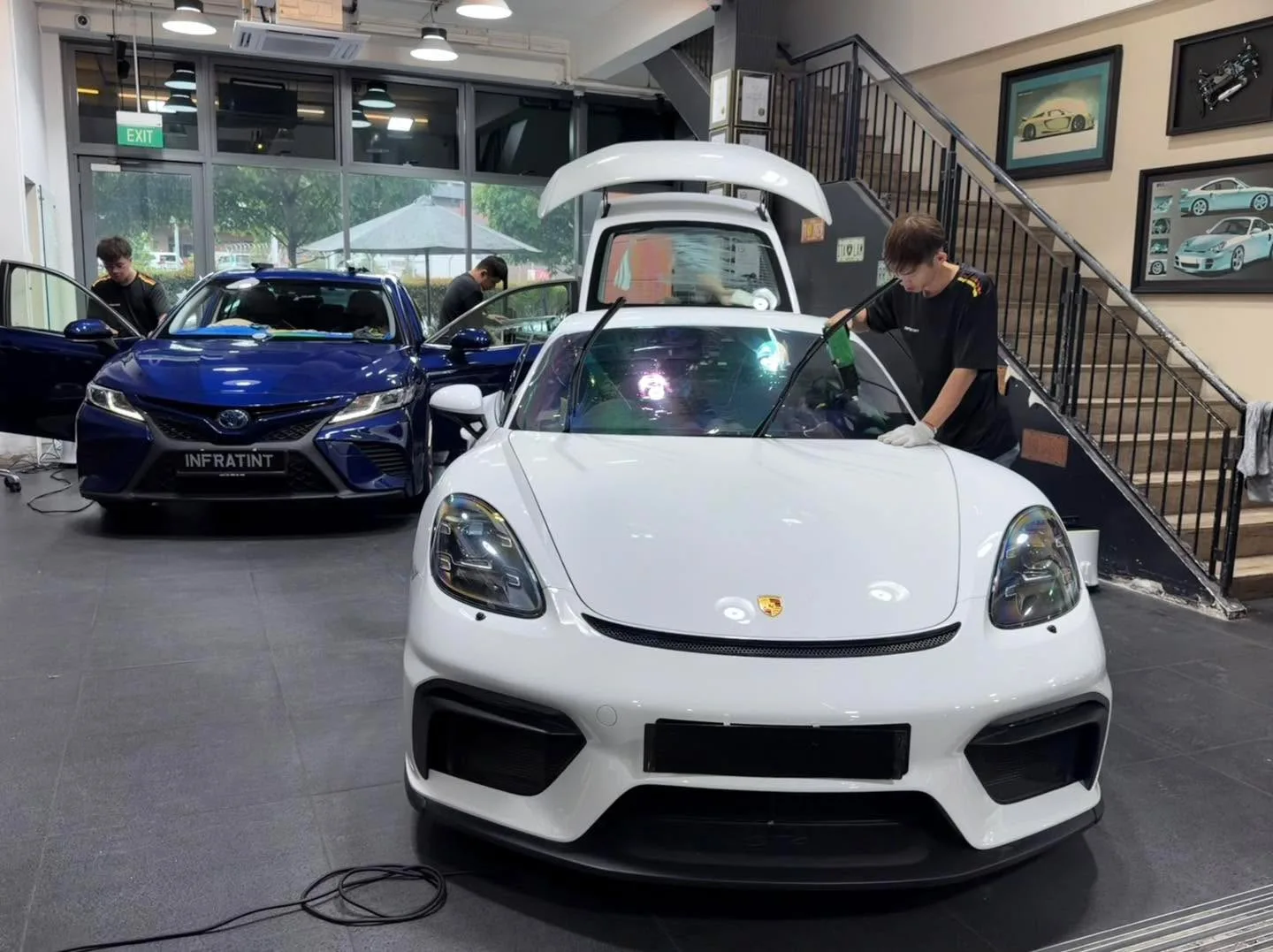 A white Porsche 911 with its roof panel open, being worked on by technicians indoors.
