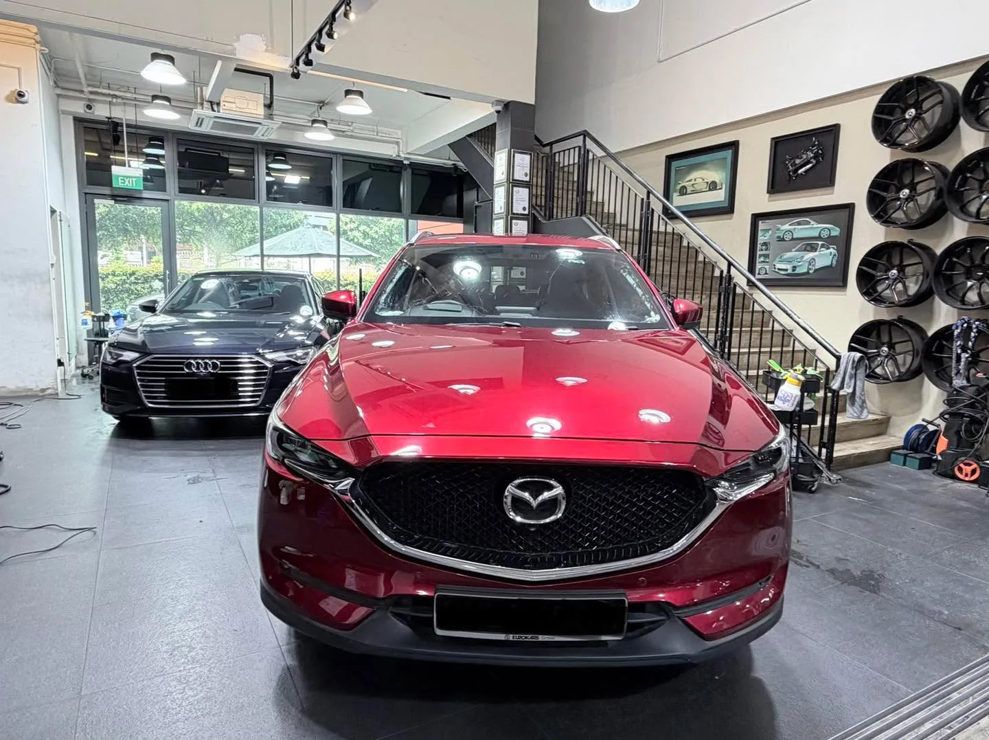 A burgundy Mazda CX-5 SUV with its boot open, parked indoors next to an Audi saloon.