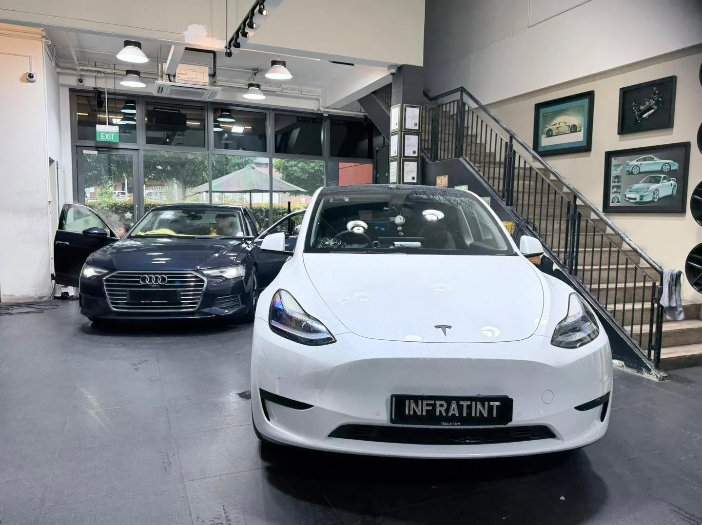 A white Tesla Model Y saloon and a dark-coloured Audi A6 saloon parked indoors.