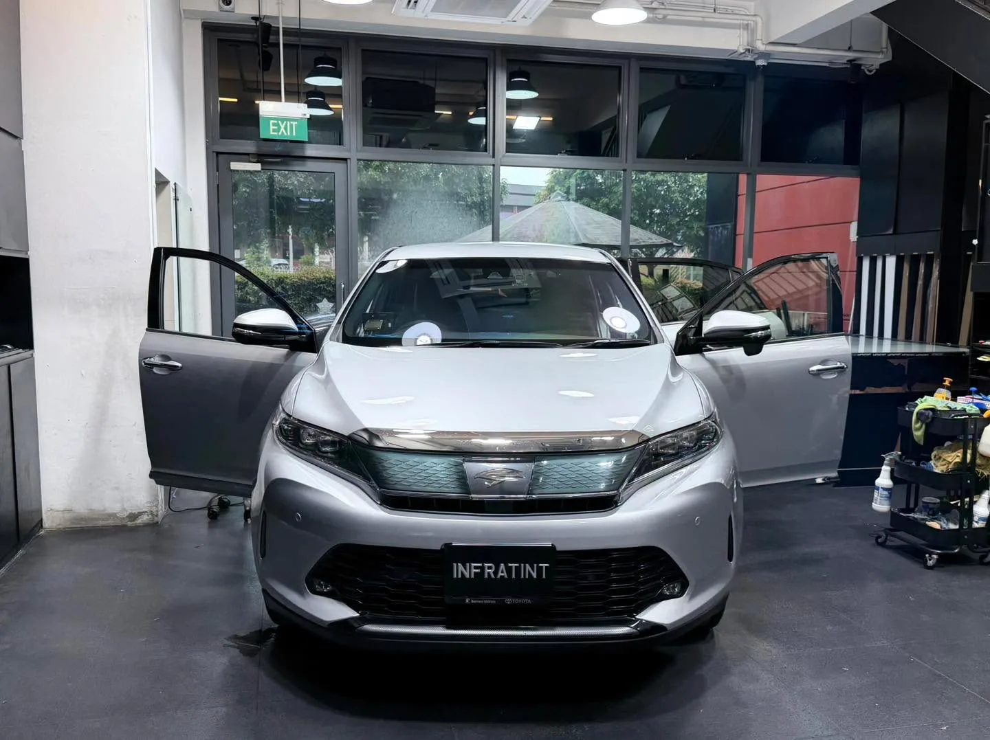A silver Toyota Harrier SUV with both doors open, parked indoors.