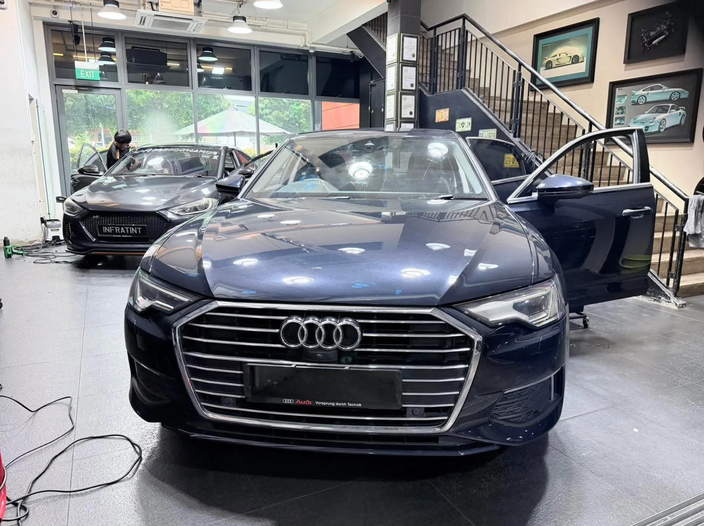 A dark blue Audi A6 saloon with doors open, parked indoors with technicians nearby.