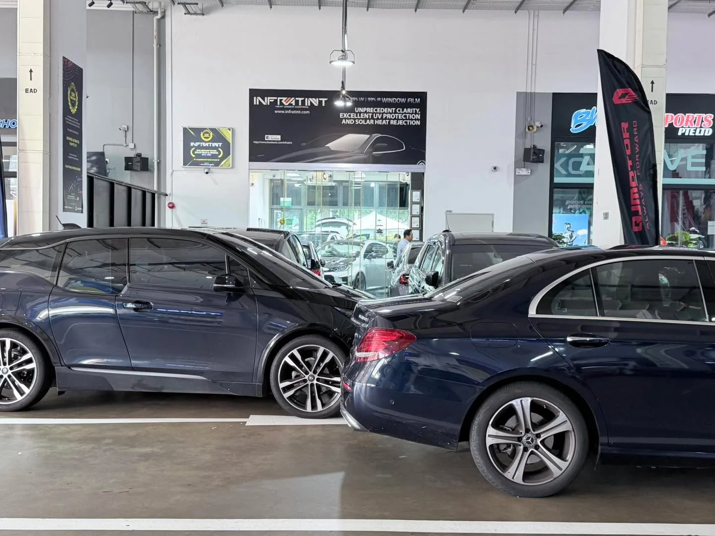 Two dark blue sedans parked side by side in the Infratint workshop.