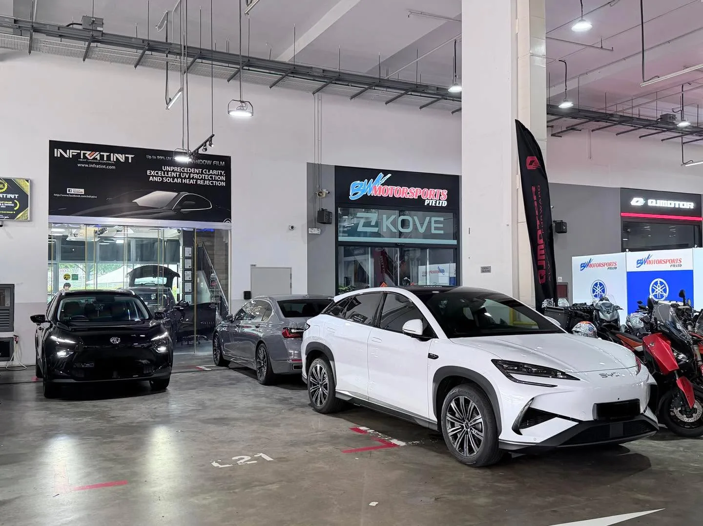 A white SUV and dark vehicles in the workshop interior with bright lighting.