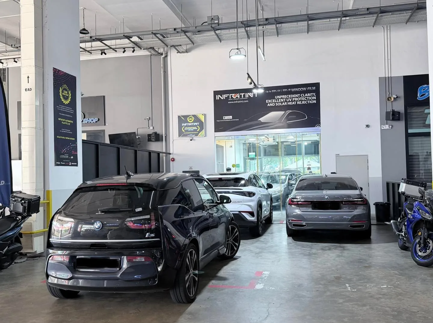 A black hatchback, a white SUV and a dark sedan parked in the workshop.
