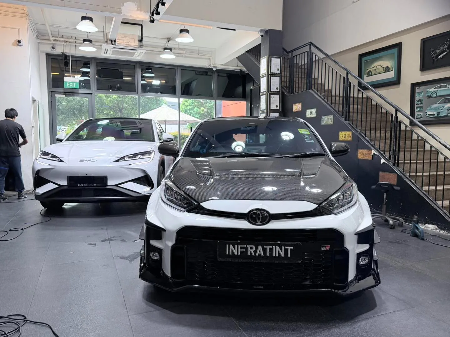 A black Toyota hatchback and a black electric sedan undergoing window tinting indoors.