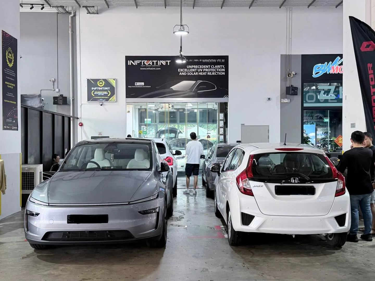 A silver Tesla Model Y and white Honda Jazz parked in the workshop alongside a white BMW sedan.