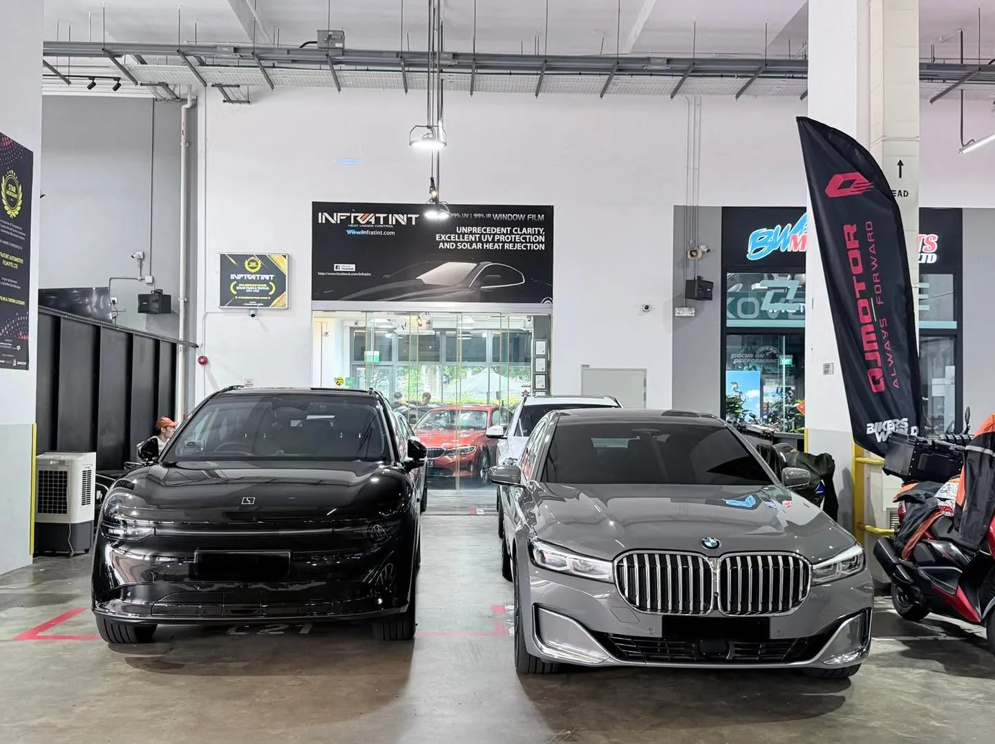 A black Tesla sedan and grey BMW sedan with distinctive kidney grille parked indoors.