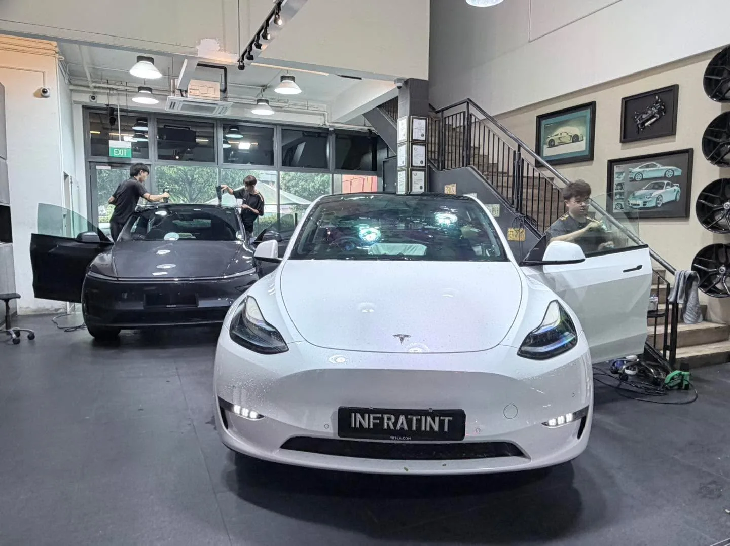 A white Tesla Model Y facing the camera in the workshop with staff nearby.